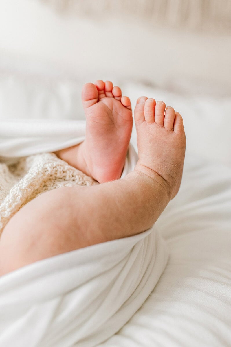 Close-up of tiny newborn baby feet on a soft bed.