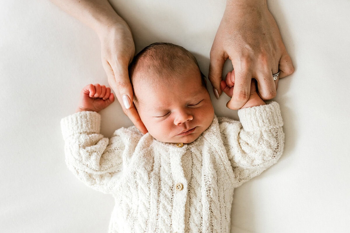 Close-up of a newborn baby with hands gently holding the baby's head.