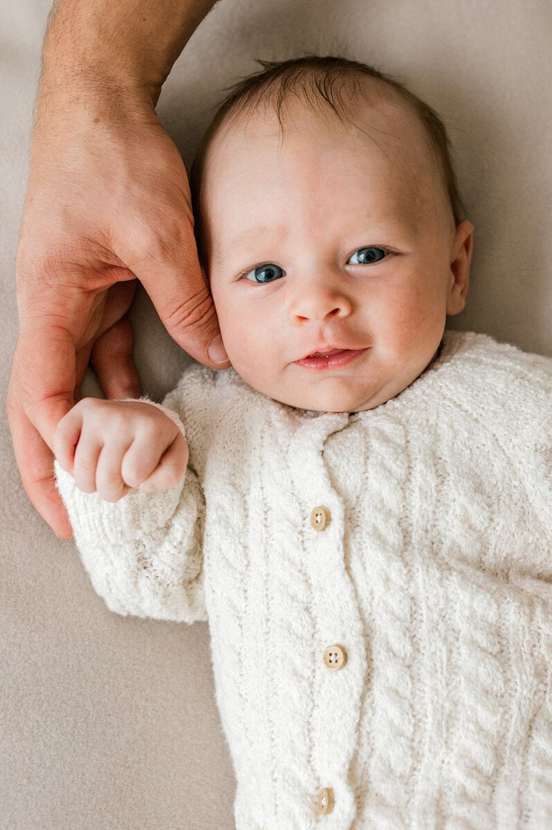Close-up of a newborn baby with blue eyes and a white knitted outfit.