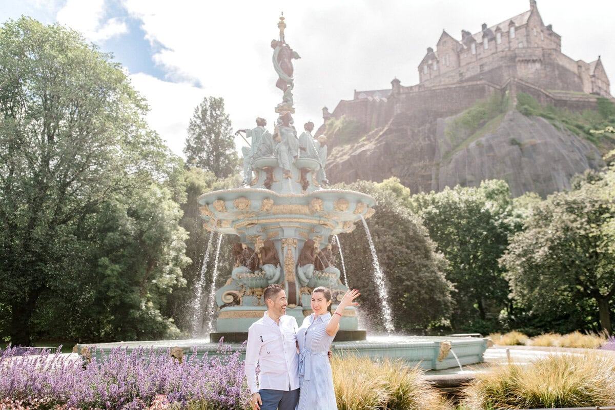 Couple taking photos near the fountain with Edinburgh Castle in background.