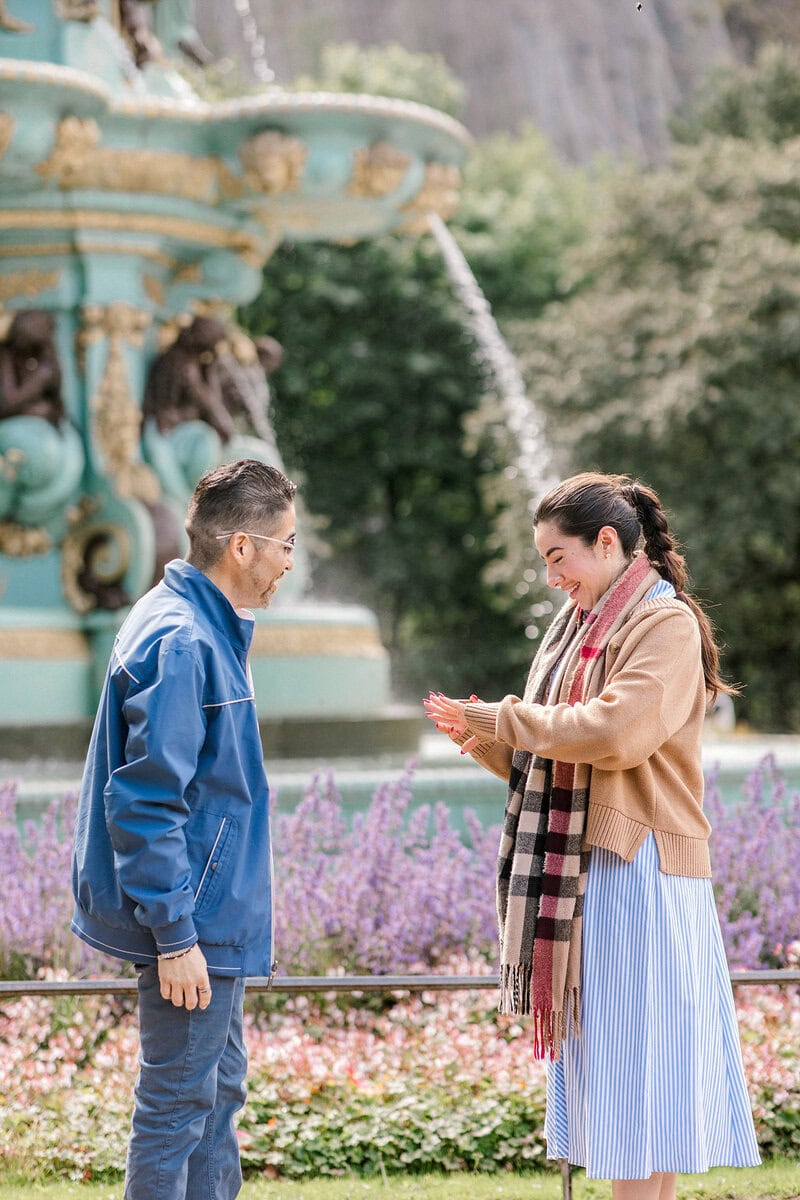 Couple proposing in front of a historic fountain in a park.