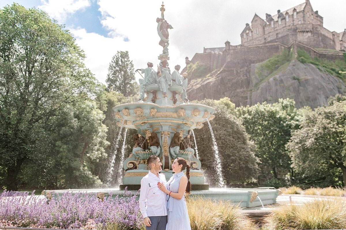Couple proposing near Edinburgh Castle fountain on sunny day.